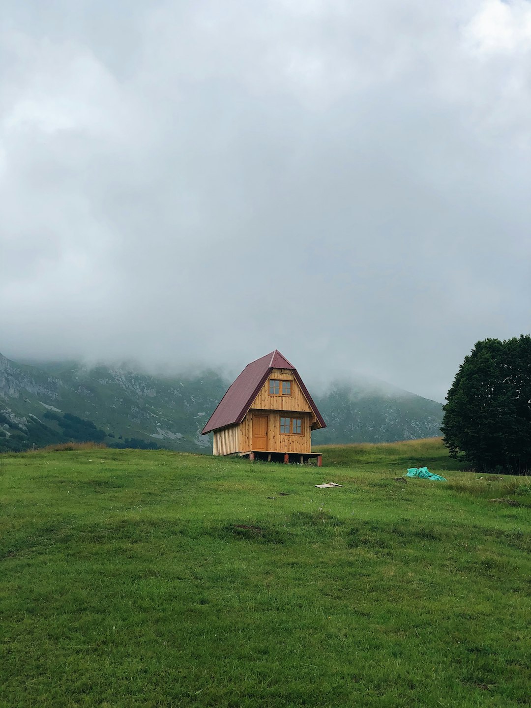 A lonely house stands in rainy cloudy weather on green grass in a village on top of a mountain in Montenegro, Zabljak.